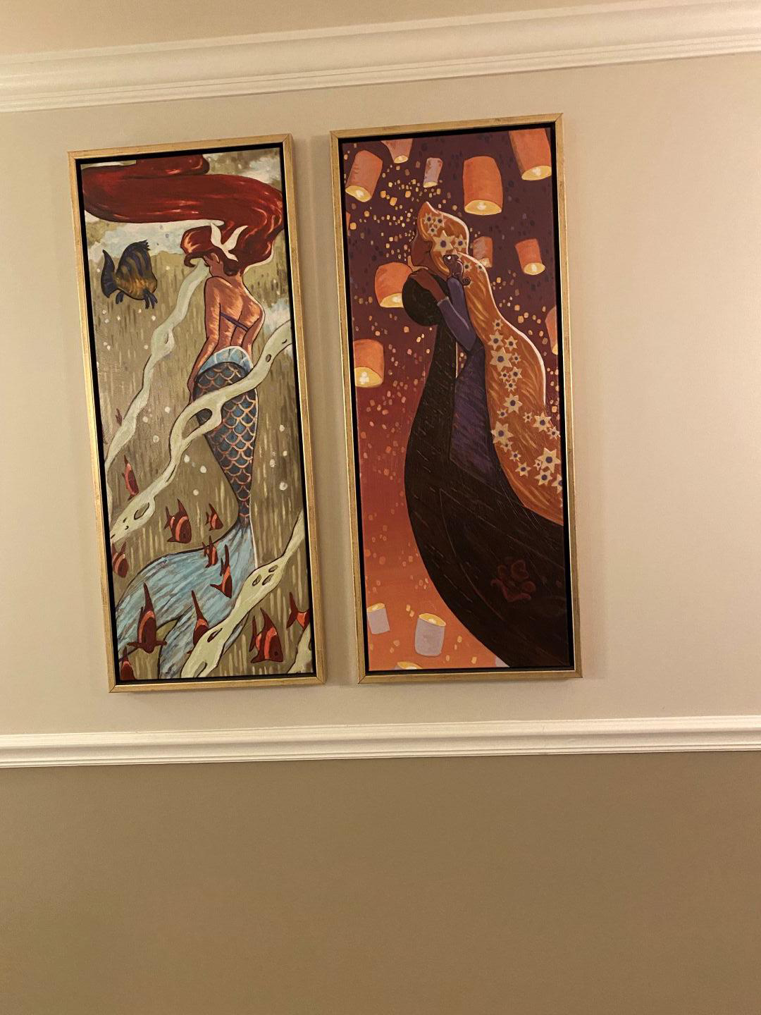 Two pictures hanging on a wall. One is of a mermaid, and the other is of a women with flowers in her hair surrounded by lanterns