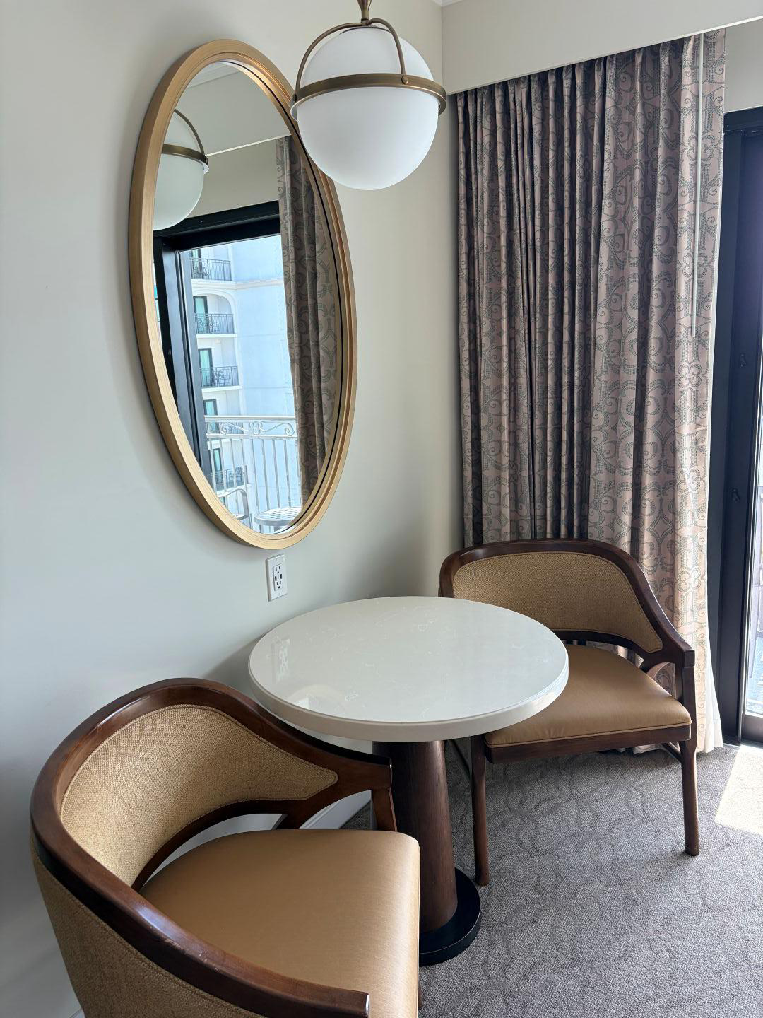 Seating area with two chairs, a table, wall mirror behind them and a ceiling light.